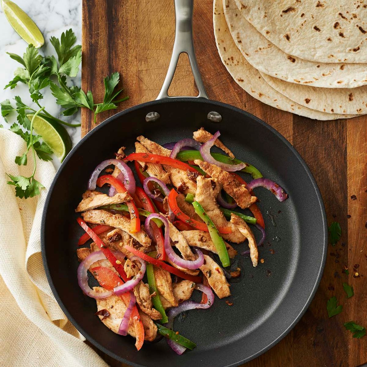 Chicken and peppers searing in a wide dark wok with lime and tortillas alongside